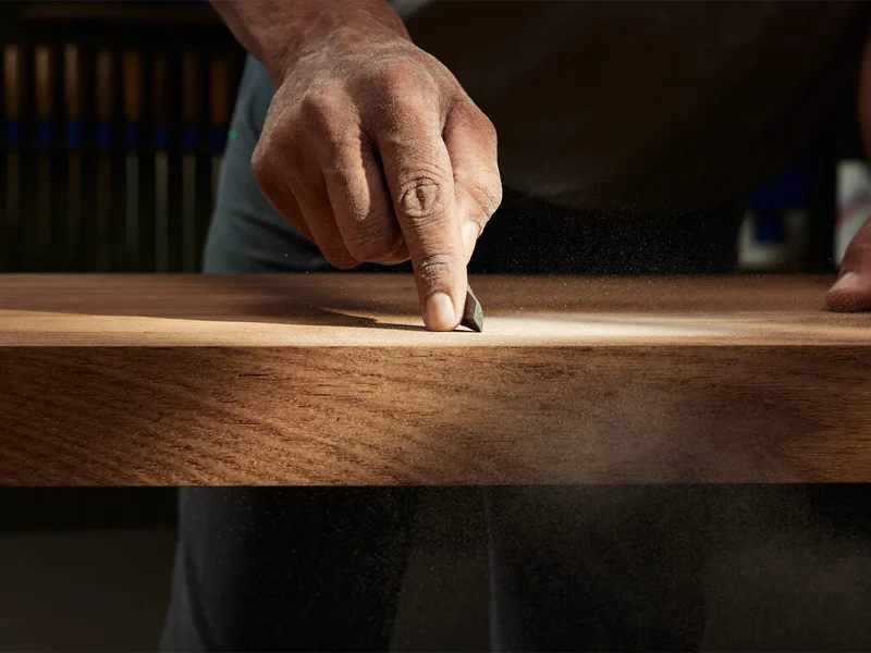 Mâini de tâmplar șlefuind muchia unui blat de stejar în atelier